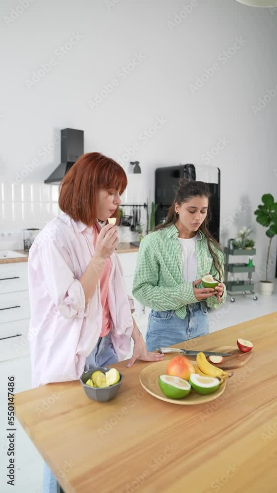 Two girlfriends cut fruit and gossip in the kitchen