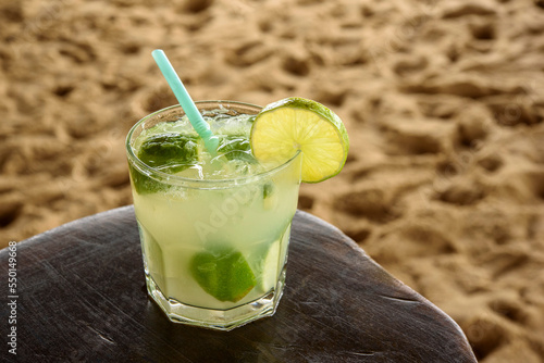 Brazilian caipirinha drink on wooden table with sandy beach background. photo
