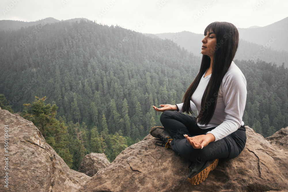 Young woman meditating and breathing on top of a mountain and forest