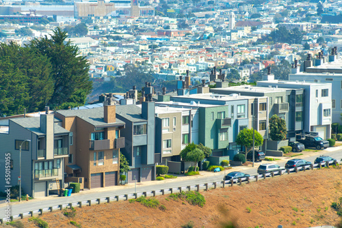 Aerial shot of multicolored row of houses with road in front and dry grassy hill and downtown city in sun background photo