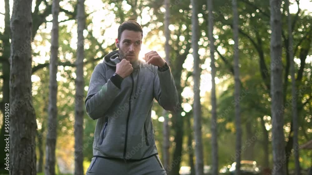 Athletic handsome man with earbuds working out and doing boxing in the forest. Athletic handsome man with earbuds working out and doing boxing in the forest.