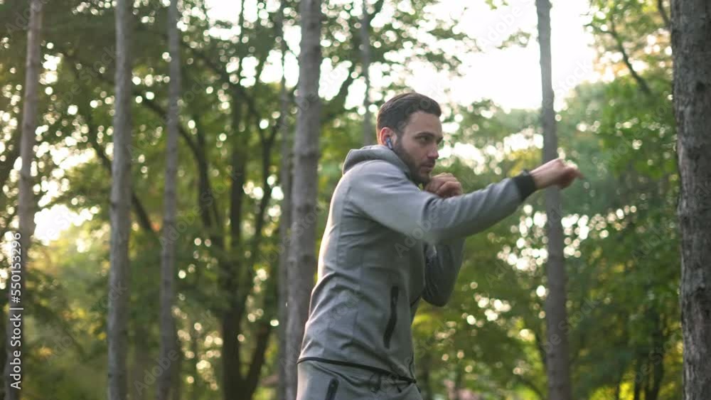 Athletic handsome man with earbuds working out and doing boxing in the forest. Athletic handsome man with earbuds working out and doing boxing in the forest.