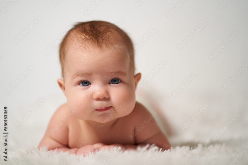 portrait of an infant with serious emotion lying on his belly against a white background portrait of an infant with serious emotion lying on his belly against a white background