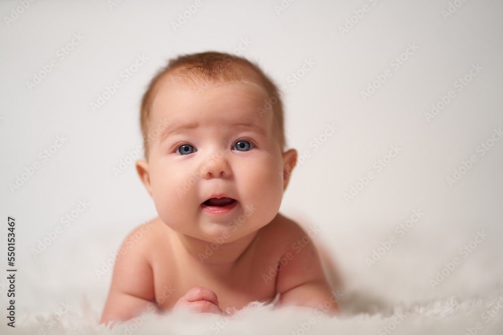 portrait of an infant with serious emotion lying on his belly against a white background