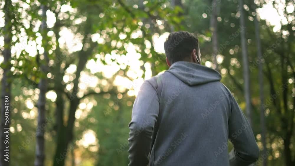 Back view of young handsome athlete with earbuds running in the forest. Back view of young handsome athlete with earbuds running in the forest.