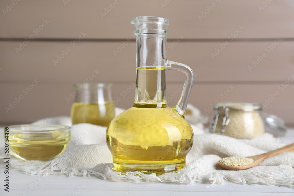 Jug of organic sesame oil and seeds on white wooden table Jug of organic sesame oil and seeds on white wooden table