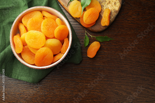 Tasty apricots with green leaves and space for text on wooden table, flat lay. Dried fruits