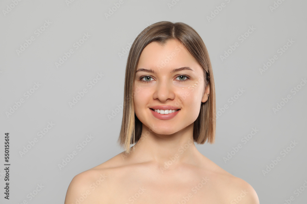 Young woman with cream around eye on light grey background Young woman with cream around eye on light grey background