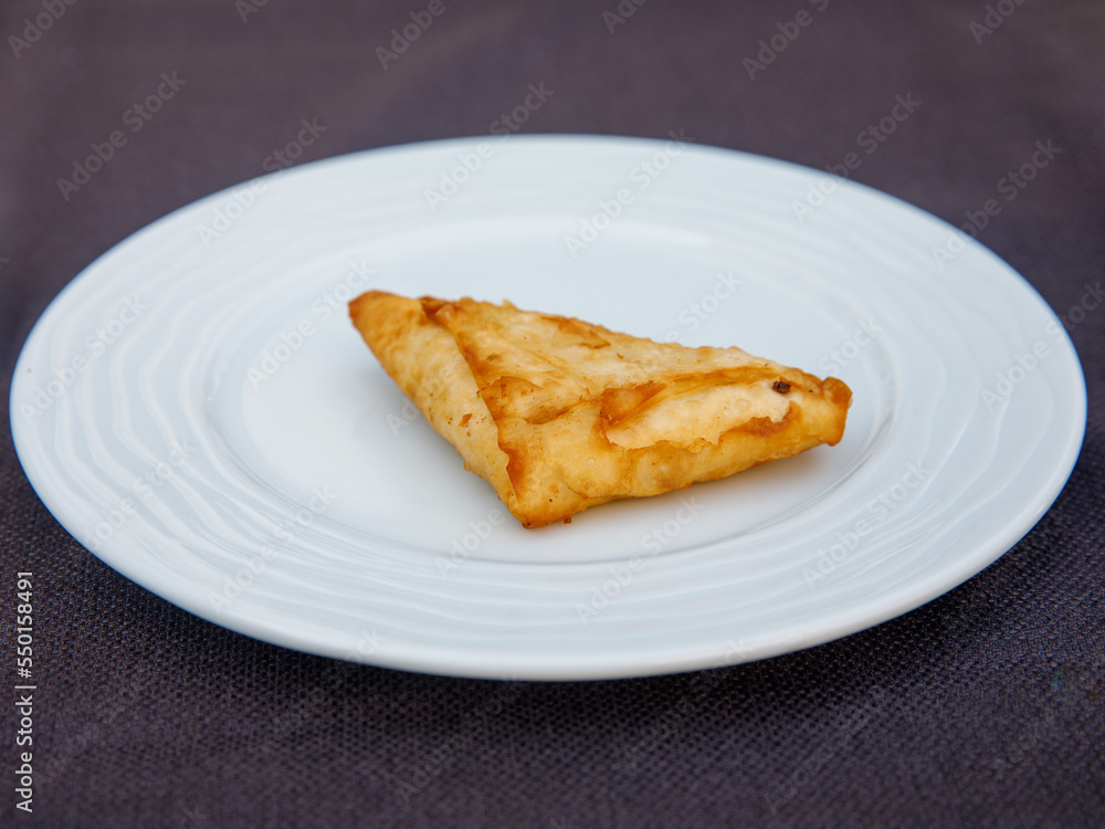 Delicious turkish pie filo pastry with greek feta cheese triangle pie close-up on white plate on the table. horizontal. Delicious turkish pie filo pastry with greek feta cheese triangle pie close-up on white plate on the table. horizontal.