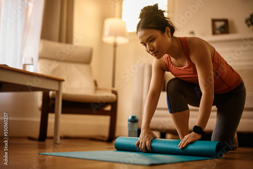 Young Asian athlete getting ready for workout and unrolling her exercise mat on floor at home.