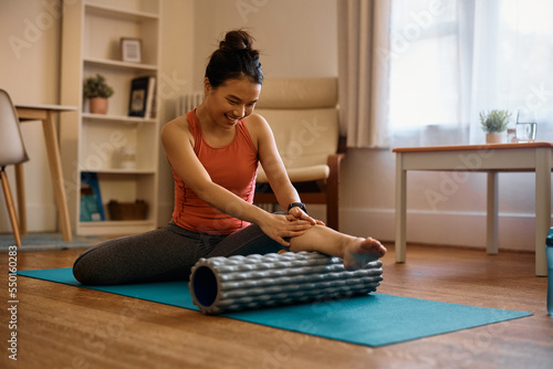 Happy Asian athlete massaging her leg on foam roller during home workout. photo