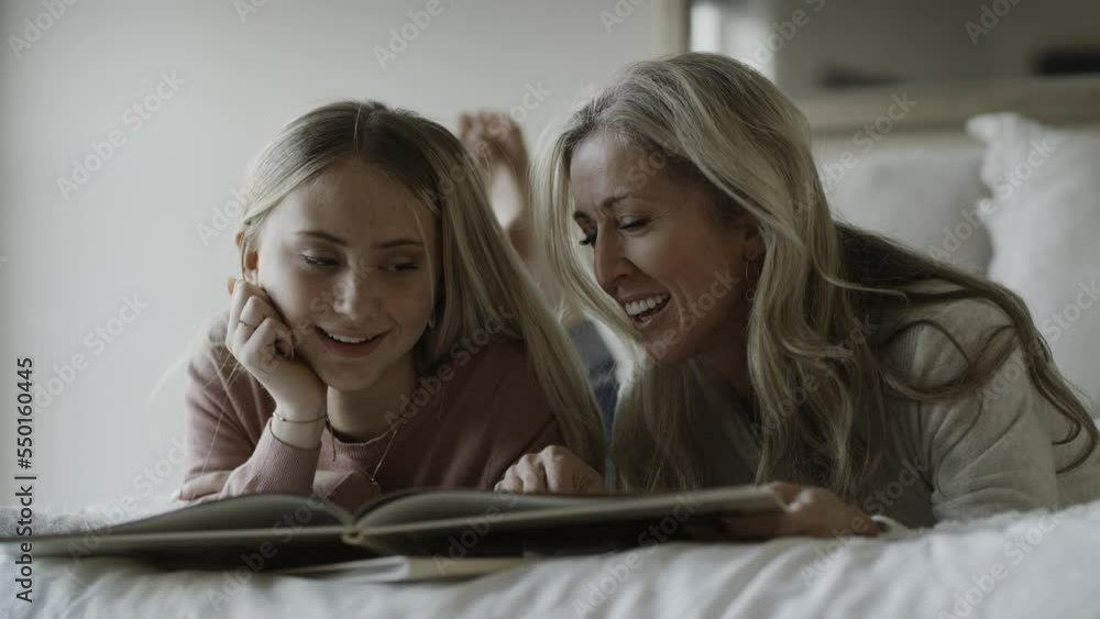 Slow motion close up of smiling mother and daughter on bed with photo album / Highland, Utah, United States Slow motion close up of smiling mother and daughter on bed with photo album / Highland, Utah, United States