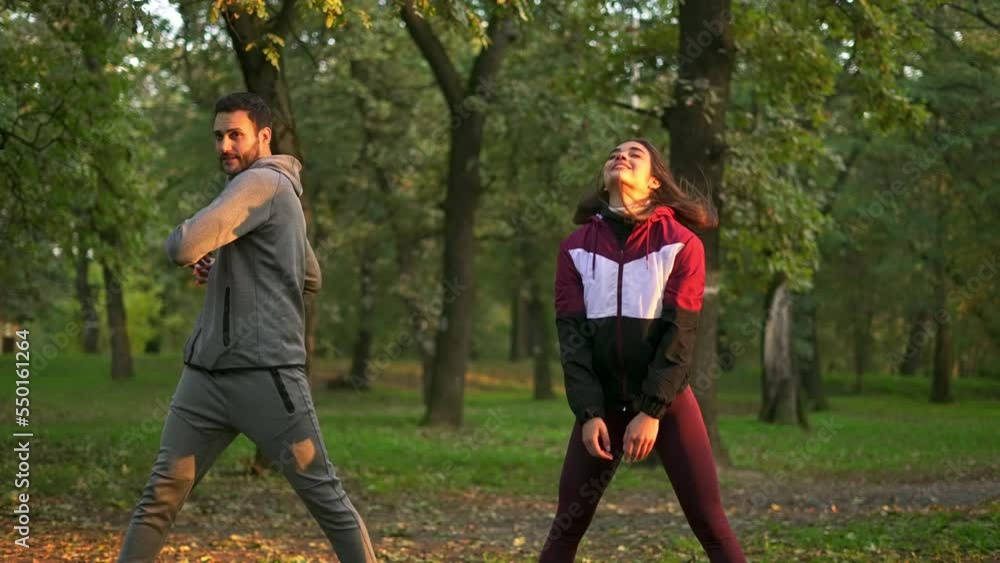 Young beautiful woman and handsome man doing arm stretching after workout in the sunny park.