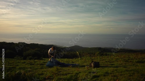 Hiker pitching a tent with ocean view at sunset photo