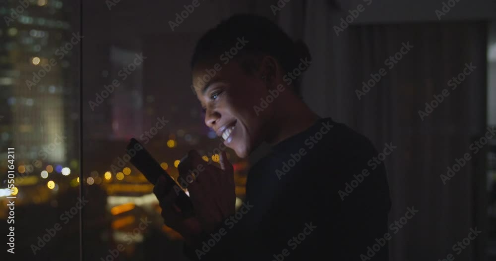 Happy african businesswoman using mobile phone by the window at night enjoy good news smiley face looking social media Happy african businesswoman using mobile phone by the window at night enjoy good news smiley face looking social media