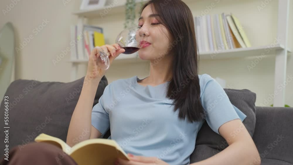 Asian beautiful woman drinking wine while reading book in living room. Asian beautiful woman drinking wine while reading book in living room.