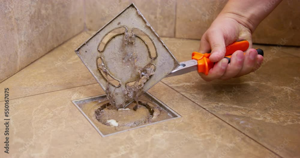 Handyman uses tools to open cover for cleaning dirty drainage in bathroom floor. Drain pipe stuck with dirt and other particles and stops water to flow Handyman uses tools to open cover for cleaning dirty drainage in bathroom floor. Drain pipe stuck with dirt and other particles and stops water to flow