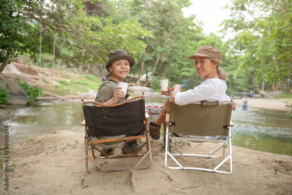 custom made wallpaper toronto digitalPleased happy mother and daughter sit camp chair looking out over river, sit near a camp and a tent, drink coffee in a pine forest. Camping, recreation, hiking.