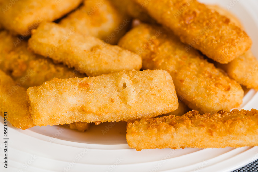 Fish sticks in a crunchy golden breading close-up on white plate on the kitchen table Fish sticks in a crunchy golden breading close-up on white plate on the kitchen table