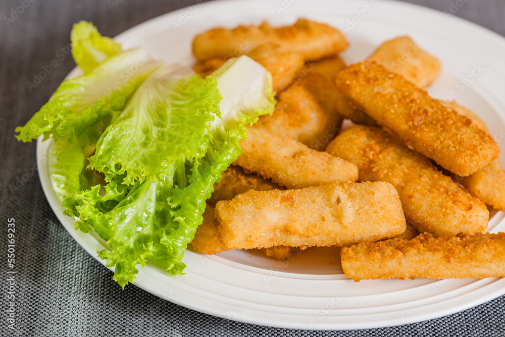 Deep-fried crunchy finger fish sticks served with green lettuce close-up on white plate