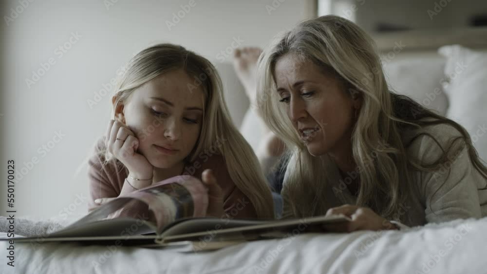 Close up of smiling mother and daughter on bed with photo album / Highland, Utah, United States Close up of smiling mother and daughter on bed with photo album / Highland, Utah, United States