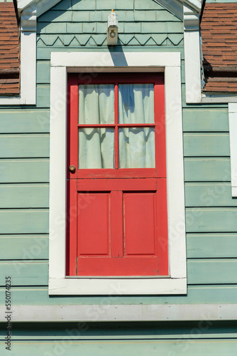 Red hidden door on side of building with white trim on the frame and green gray exterior horizontally slatted wood or timber house