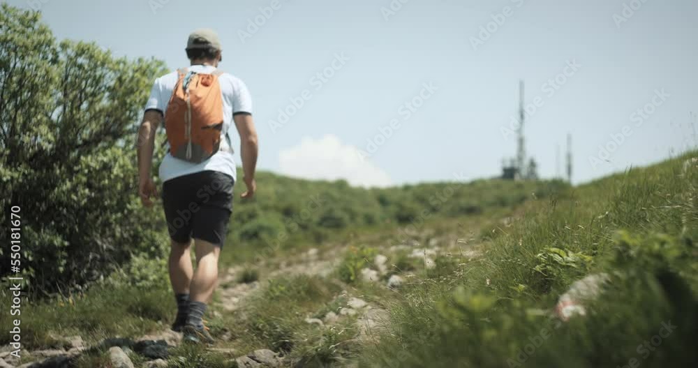 Hiker with an orange backpack walking on the rocky path towards the radio tower on mountain Nanos. Low perspective camera shot. Hiker with an orange backpack walking on the rocky path towards the radio tower on mountain Nanos. Low perspective camera shot.