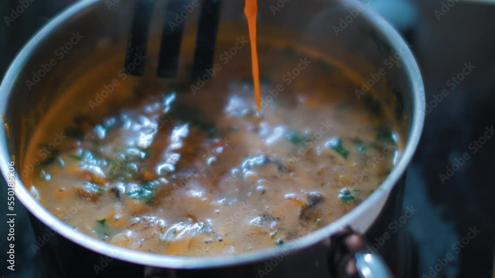 Bright orange soup with meat and vegetables is bubbling. Tasty and spicy Asian Tom Yam soup in metal saucepan on cooking stove. Bright orange soup with meat and vegetables is bubbling. Tasty and spicy Asian Tom Yam soup in metal saucepan on cooking stove.