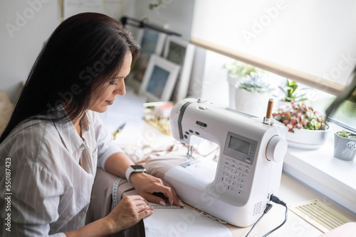 Foto Female skilled dressmaker sews fabric garment on sewing machine enjoy work at ho
