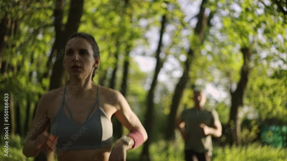 Close up of a young athletic woman jogging in the sunny forest. Fit man running in the background. Helathy lifestyle concept.Slow motion. Close up of a young athletic woman jogging in the sunny forest. Fit man running in the background. Helathy lifestyle concept.Slow motion.