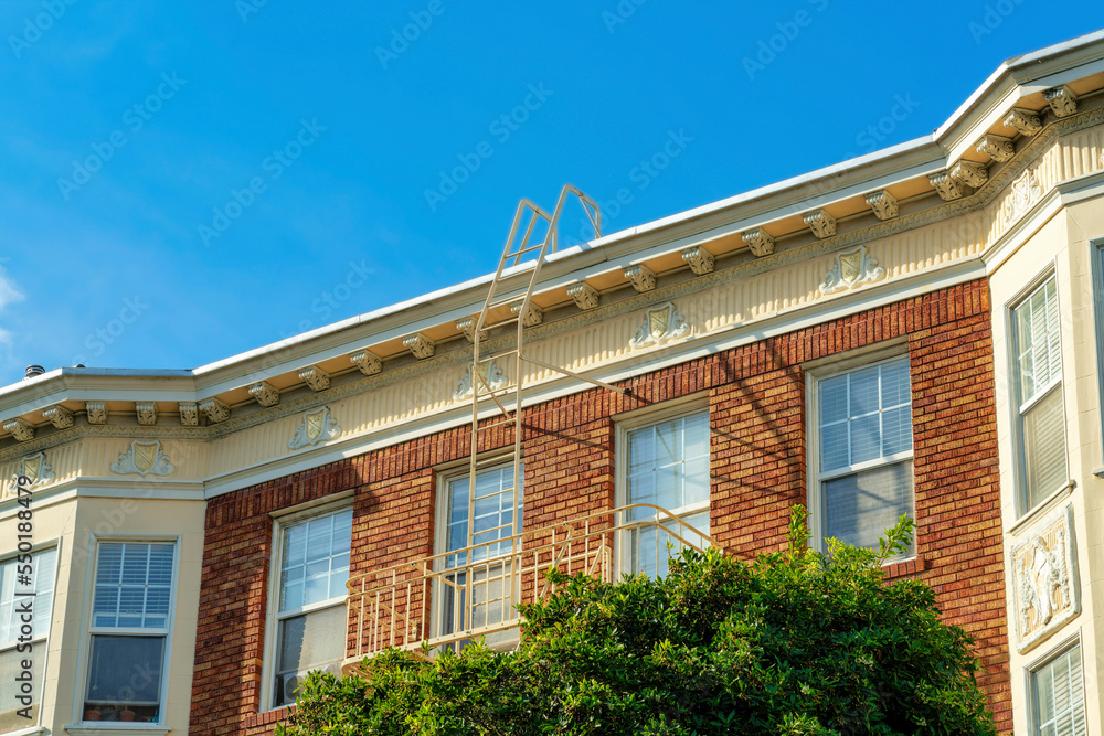 Modern brick building facade with white accent paint in the daytime sun with front yard tree and blue sky background