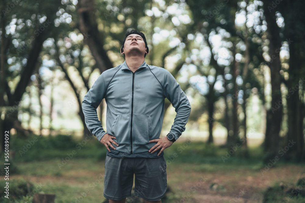 A man wearing earphones and  stretching before running. Young man workout before fitness training in the forest. Healthy and exercise warming up.