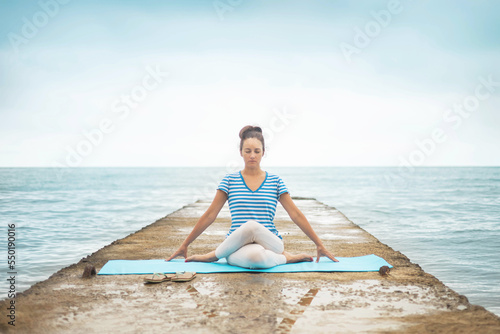 Active female yogi instructor practicing gomukhasana position sitting on rug stones aloe plant park