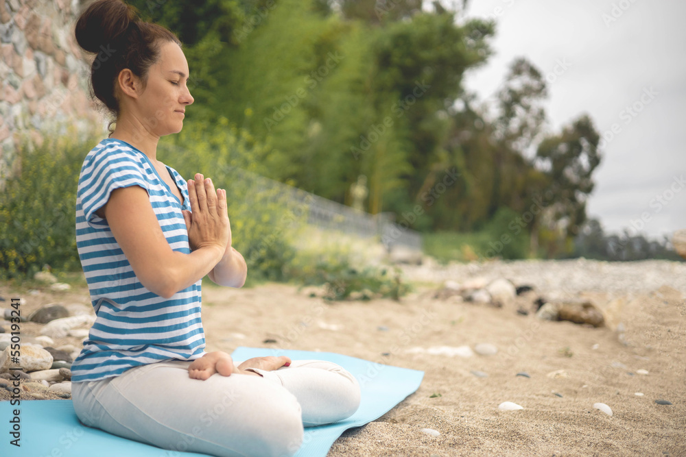 Concentrated woman sitting in lotus position yoga at summer