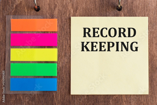 RECORD KEEPING text on a yellow card on a wooden background, business concept