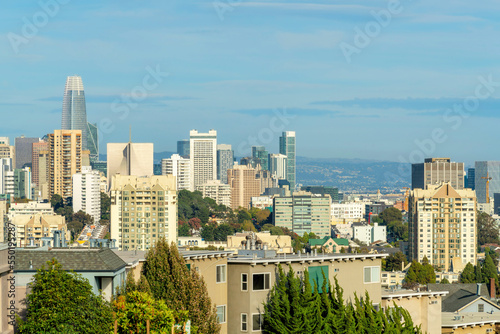 Sprawling city with downtown buildings and structures in evening sun with trees and foliage and foggy blue sky with moutains