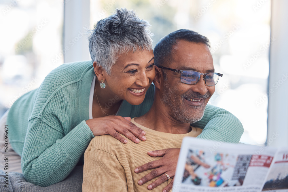Love, senior couple and reading newspaper in living room of home. Retirement, relax and happy elderly man and woman embrace in house, hugging or cuddle while looking at news article or story in house