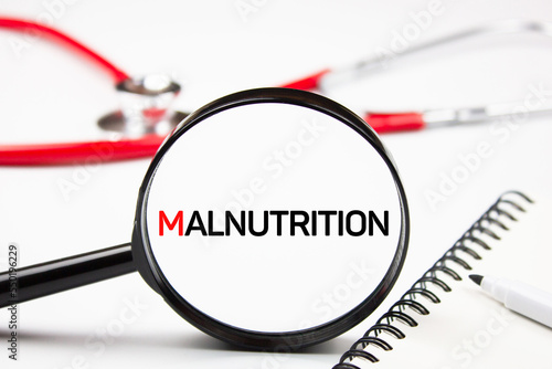 The word malnutrition through a magnifying glass on the background of a stethoscope. Problem of malnutrition concept. photo