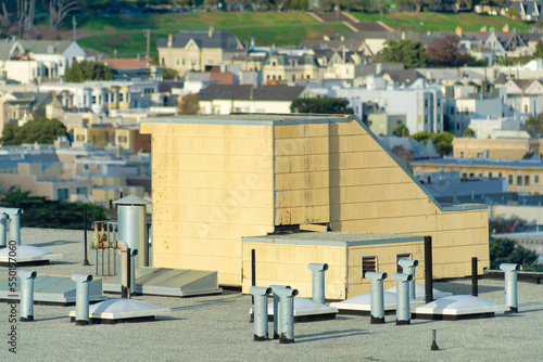 Roof access staircase with chimney pipes and buildings and houses in background in midday sun