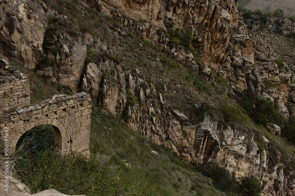 Famous aul-ghost  Gamsutl' - ruin of ancient stone city in Caucasian mountains in summer. Majestic destruction and abandoned stone castle with arches on cliff with canyon around and green mountains.