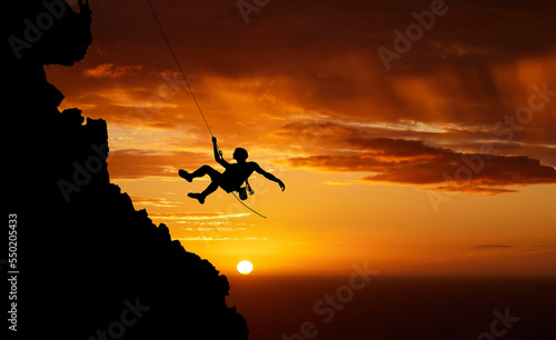 Sunset sky abseiling, mountain silhouette and hiking man hanging on shadow rope. Fitness risk, adventure freedom challenge and strong, surreal nature adrenaline and cliff climbing on orange landscape