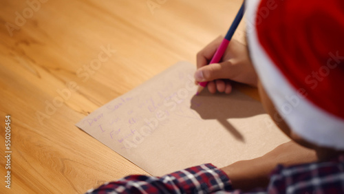 LittleAfrican-American boy in santa hat writing letter for santa on christmas eve