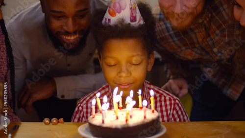 Happy African-American preteen boy blowing out candles on birthday cake celebrating with family photo