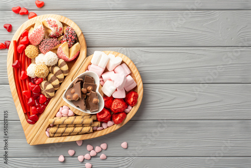 Valentine's Day concept. Top view photo of wooden heart shaped serving tray with sweets plate chocolate jelly candies and cookies on grey wooden desk background with blank space