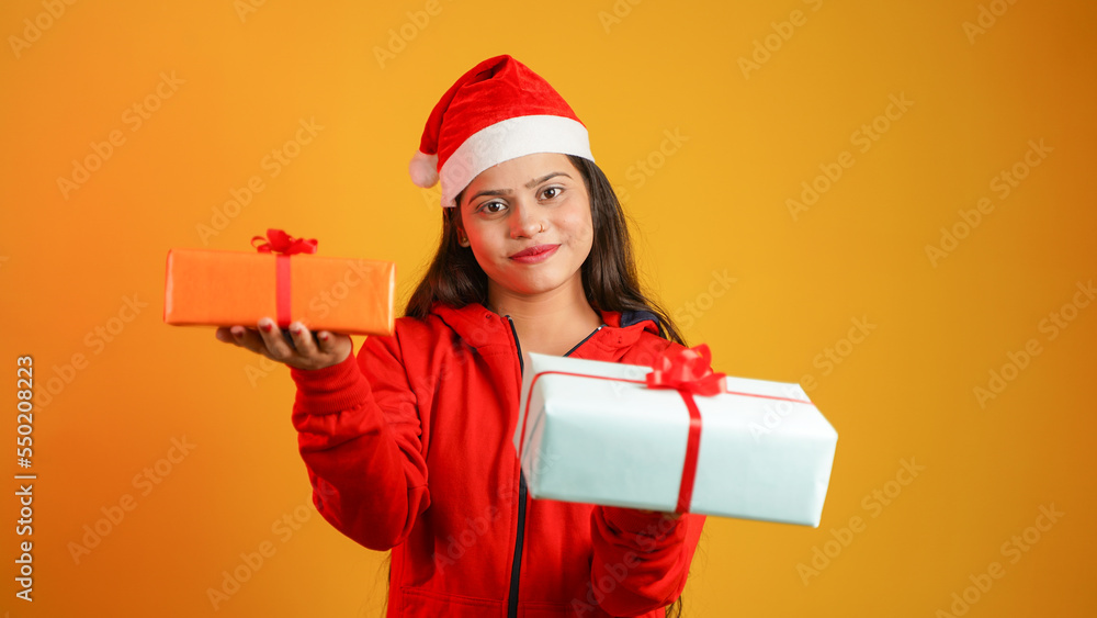 Beautiful young woman with Christmas gift box, Asian Indian girl wearing Santa cap isolated over colour studio background Beautiful young woman with Christmas gift box, Asian Indian girl wearing Santa cap isolated over colour studio background