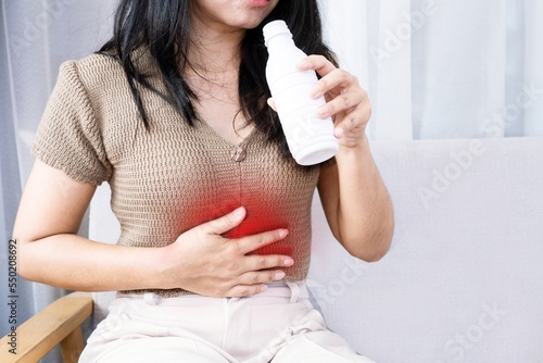Asian woman taking antacid medicine gel to treat her heartburn from gerd and stomachache photo