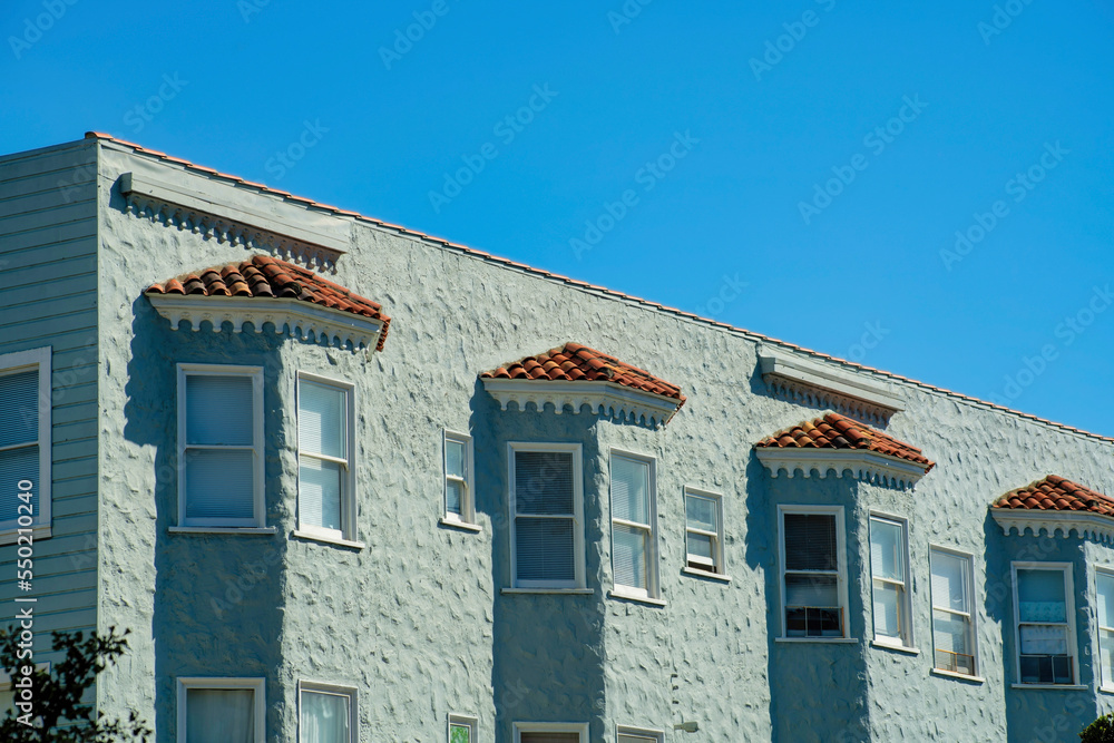 Row of apartment units on green gray building or structure in late afternoon sun with red adobe tiles and flat roof