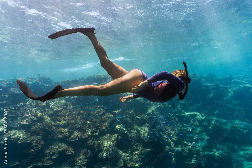 Woman snorkeling in Coral Bay Western Australia, lots of corals all around with clear blue water that has many sun rays shining through. Woman is freediving coral reef in western Australia. 