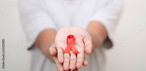female hands with red aids awareness ribbon, HIV AIDS Badge to spread HIV AIDS Awareness, Healthcare, medicine and AIDS awareness concept.