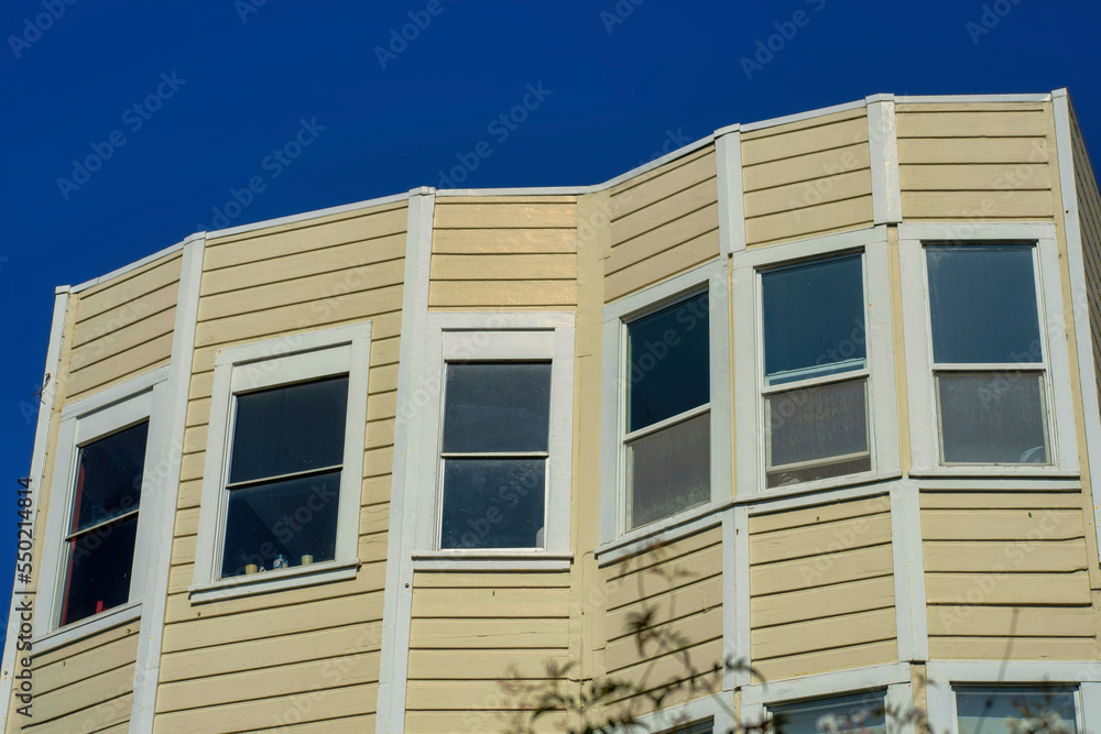 House facade with beige and slatted wood pannel exterior on home with front yard foliage and dark blue sky background House facade with beige and slatted wood pannel exterior on home with front yard foliage and dark blue sky background